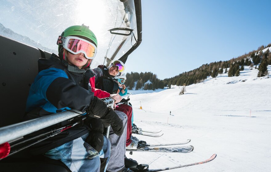 Familie sitzt mit Skiern auf dem Sesselift in Lenzerheide | © Lenzerheide Bergbahnen AG