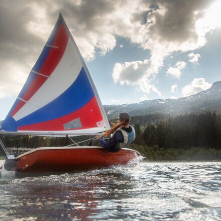 Junge Frau beim sportlichen Segeln auf dem Heidsee vor dramatischer Bergkulisse mit Sonne und Wolken. | © Sundroina Pictures