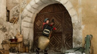 Schellen-Ursli mit seiner Glocke vor einer Tür | © Kultur am Pass